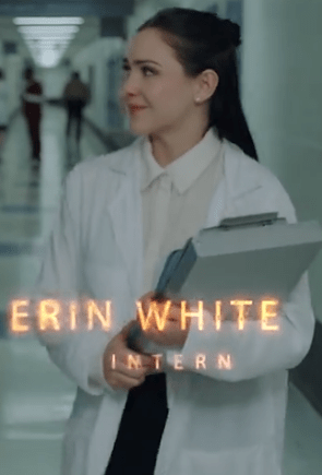 A female intern in a lab coat holding a folder, walking through a hospital corridor.